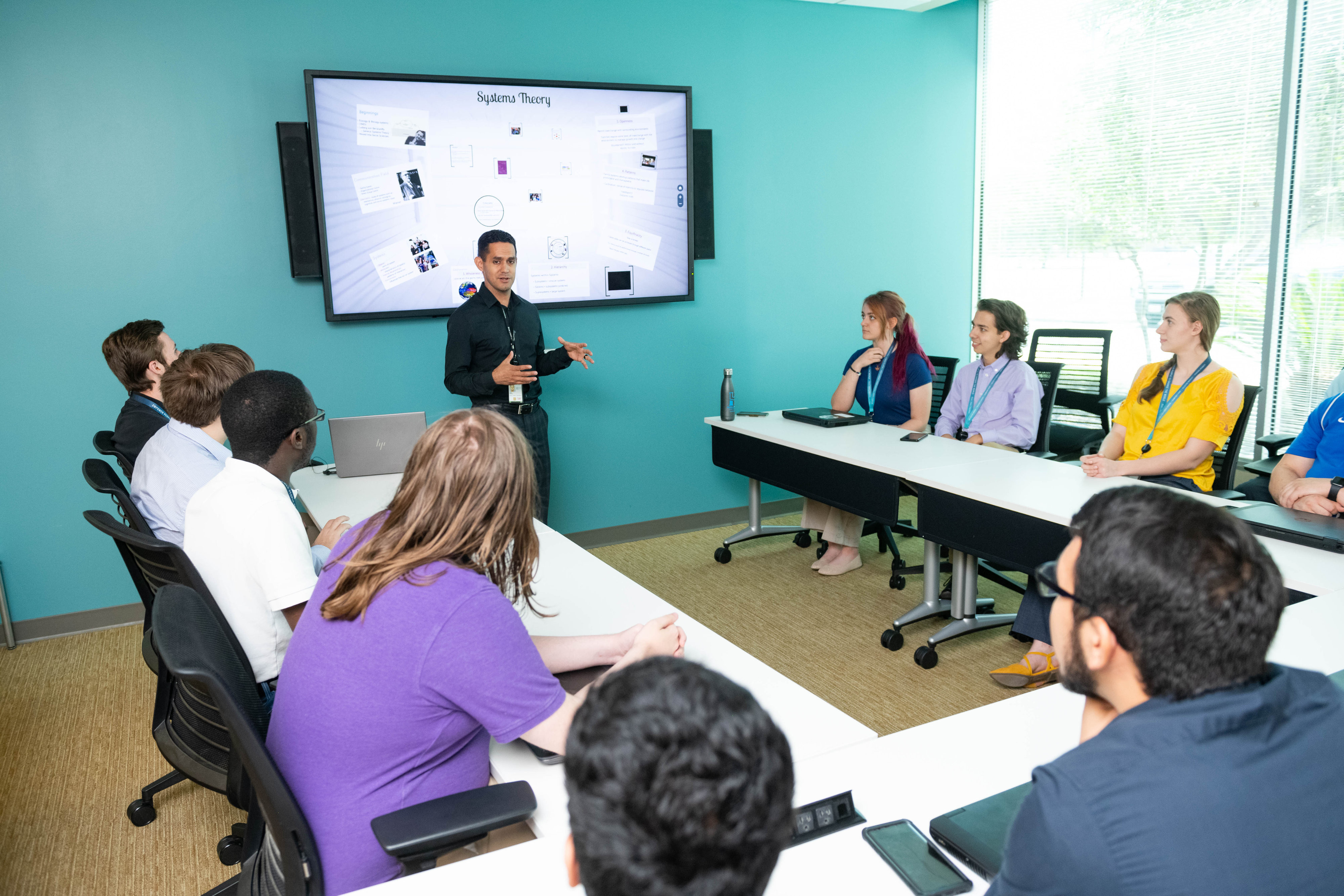 Photo of men and women watching a presentation on a screen in a conference room like room
